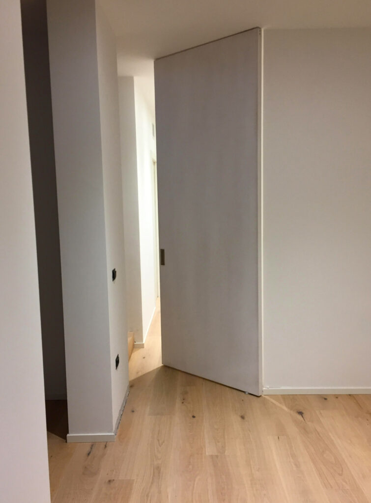 Porta a bilico bianca con apertura pivot installata in un ambiente moderno, integrata nella parete per un effetto minimale e pulito.